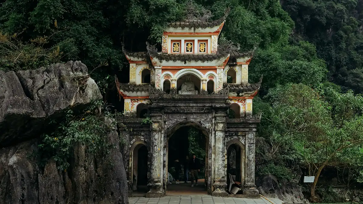 Stone entrance gate to Bich Dong Pagoda surrounded by limestone cliffs and trees
