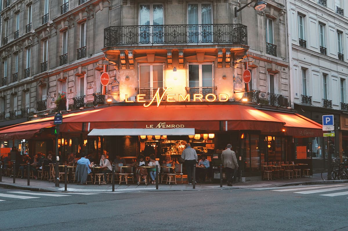 Paris cafe in Le Marais at night with people dining and warm street lights