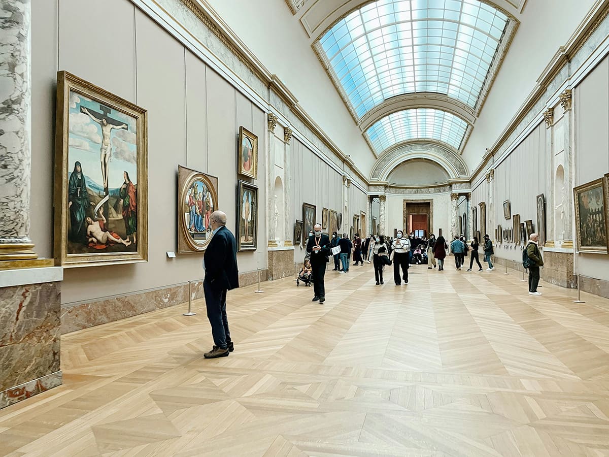 Visitors exploring art gallery inside Louvre Museum in Paris with classical paintings