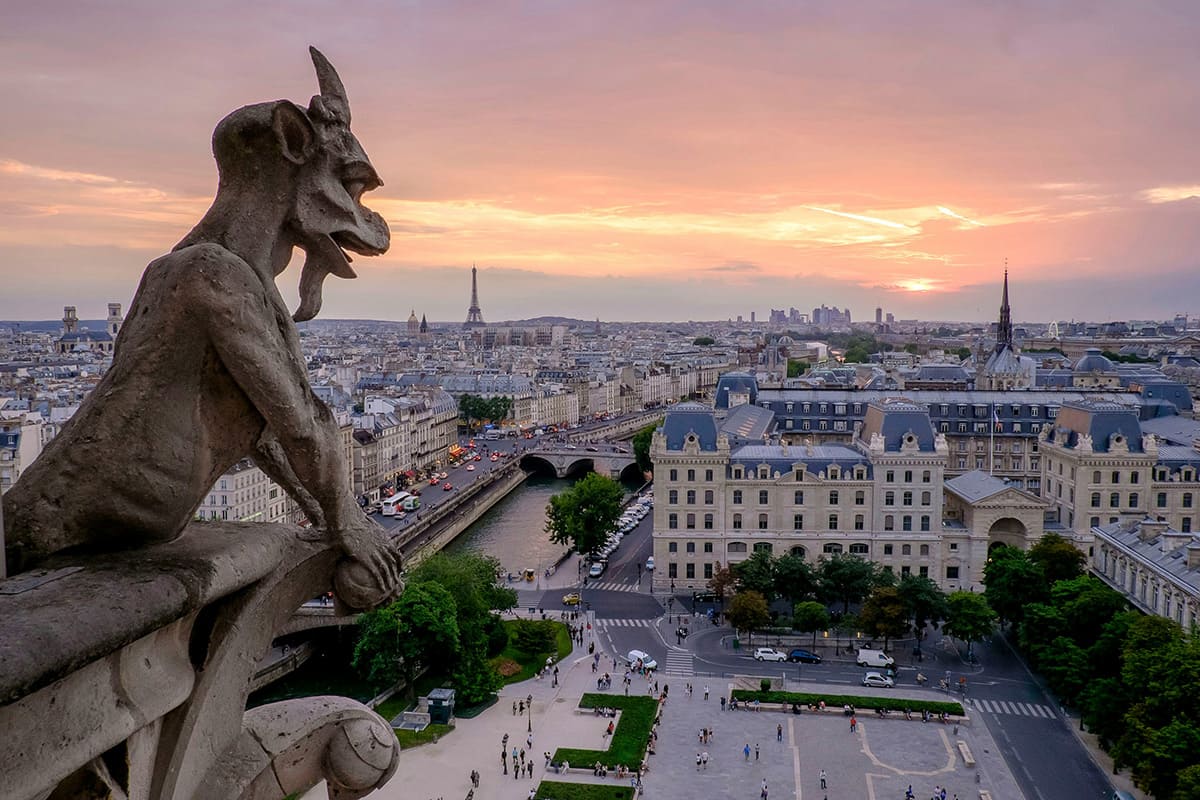 Notre Dame gargoyle overlooking Paris skyline with Eiffel Tower at sunset