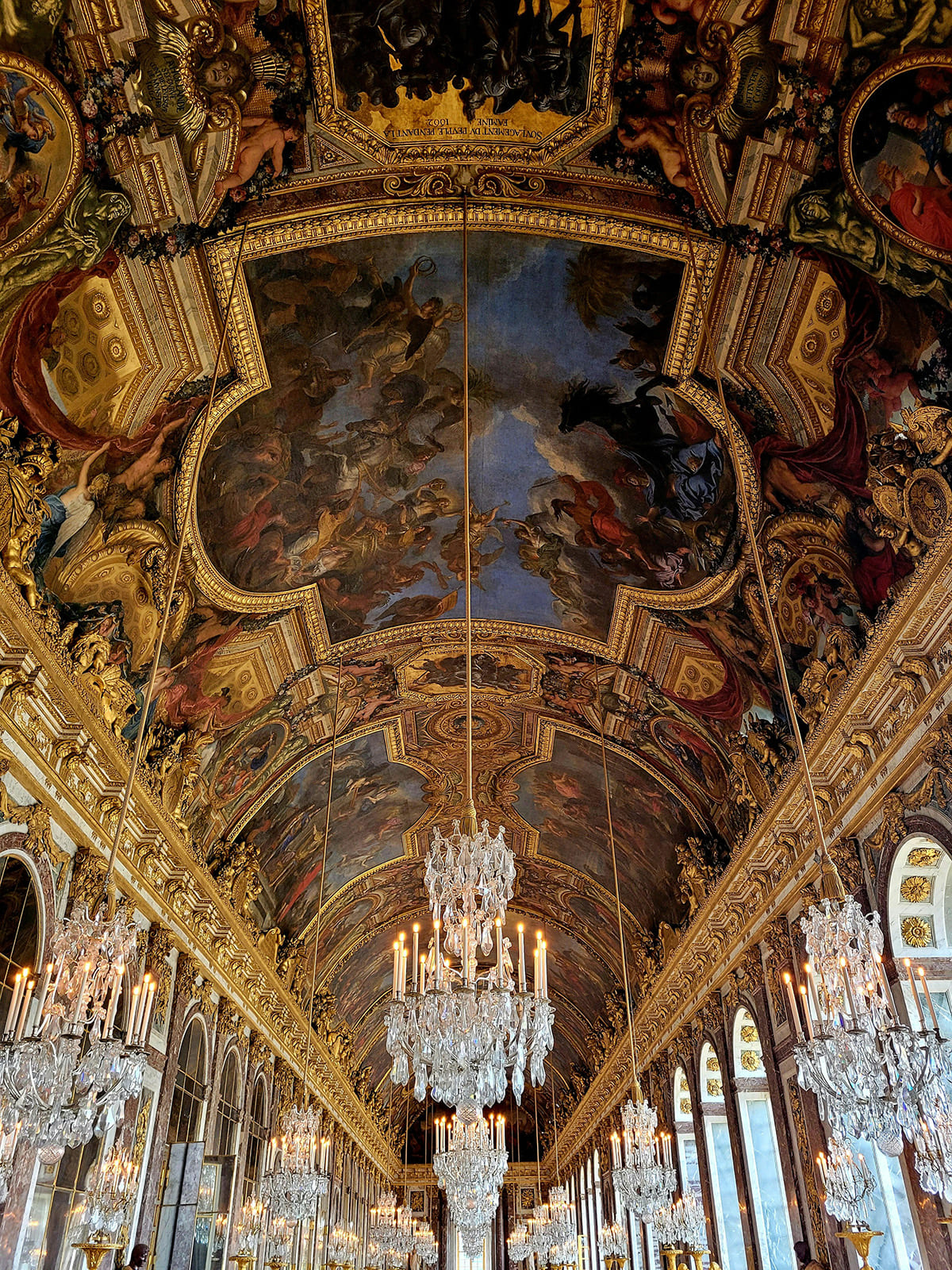 Hall of Mirrors in Versailles with chandeliers and detailed ceiling artwork