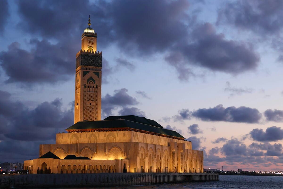 Hassan II Mosque illuminated beside Casablanca's Atlantic waterfront at dusk