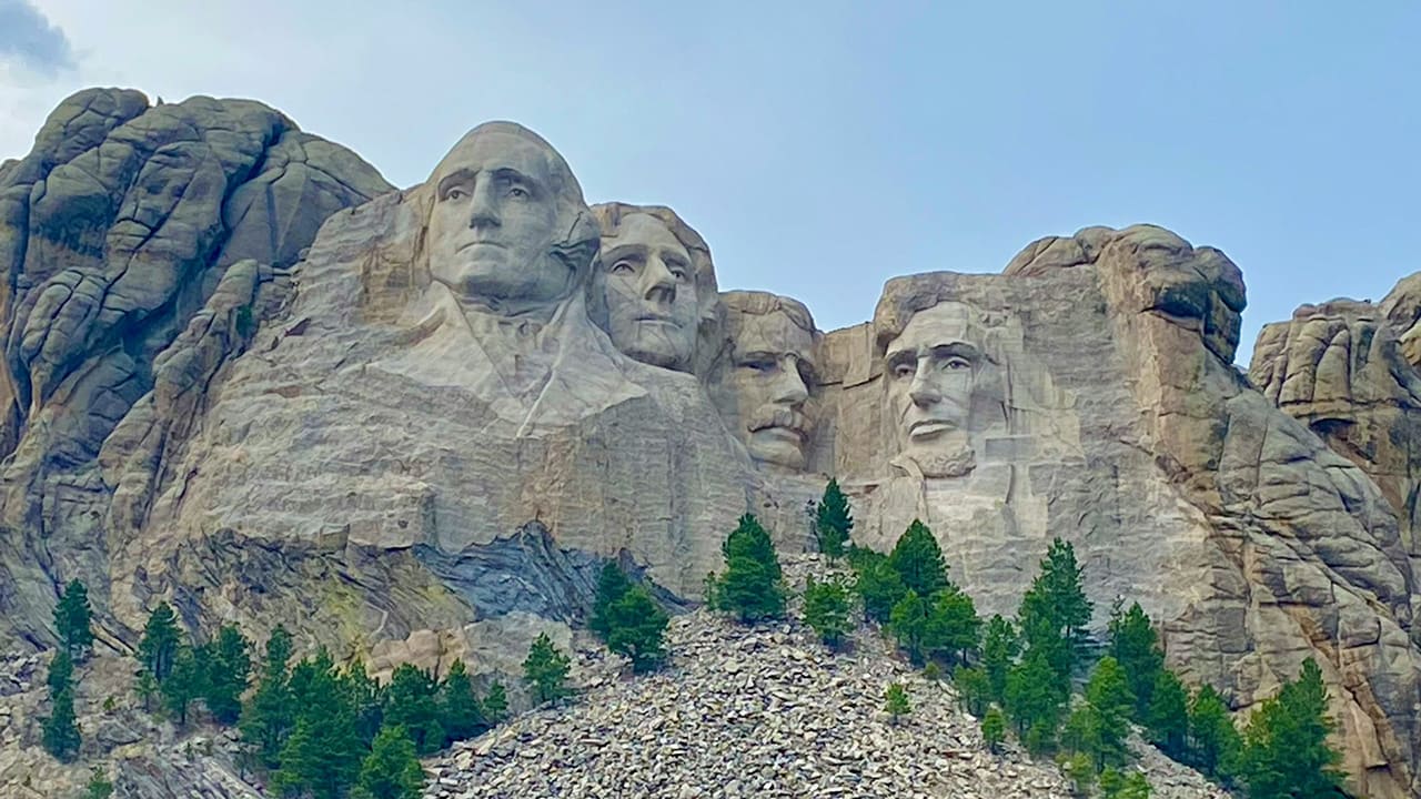 A wide landscape view of Mount Rushmore National Memorial featuring the four carved presidents under a clear blue sky.