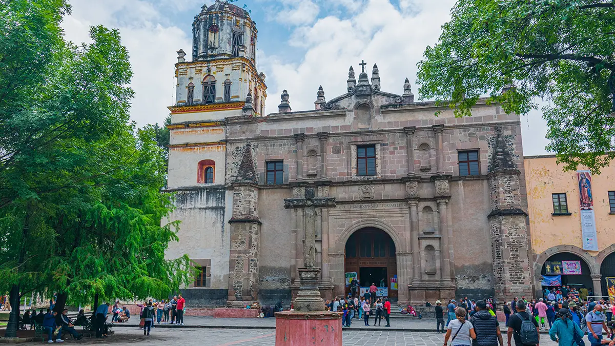 Iglesia de San Juan Bautista frente a una plaza arbolada de Coyoacán.