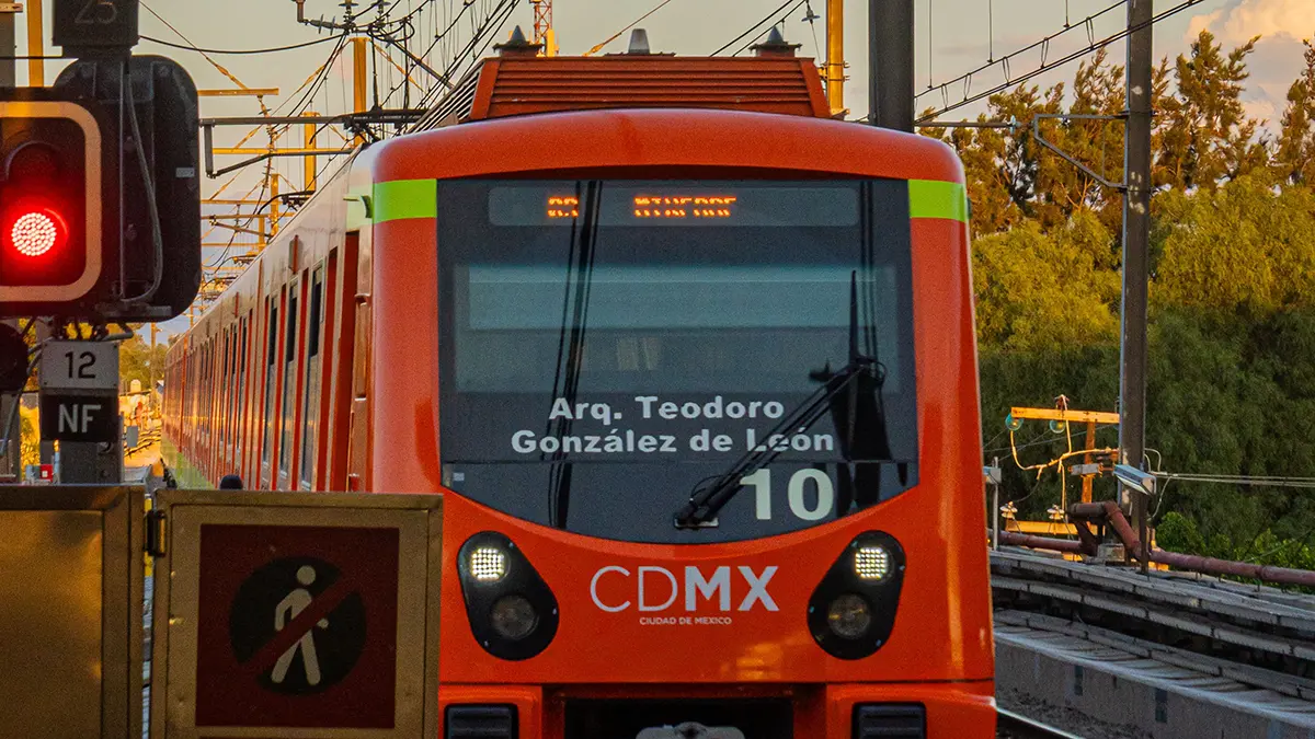 Vehículo ferroviario naranja con las siglas CDMX en una vía con cables eléctricos aéreos.