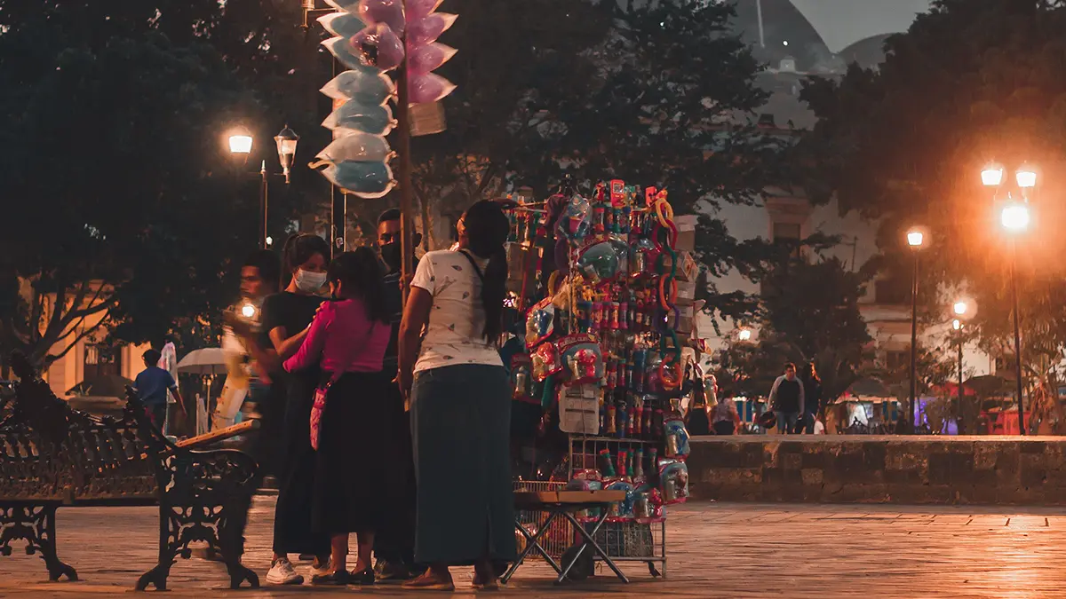 People gathered beside a street vendor in an Oaxaca plaza at dusk