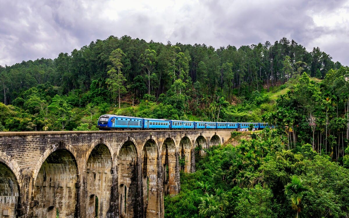 Un tren azul cruzando el puente de los Nueve Arcos, rodeado por un bosque verde en Ella, Sri Lanka