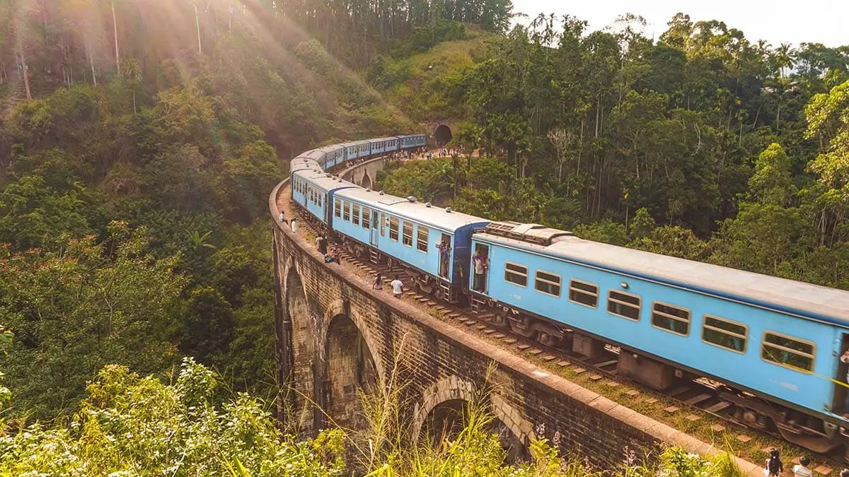 Tren azul curvando sobre un puente de piedra en la región montañosa de Sri Lanka